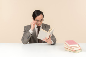 An asian teacher in a checkered suit, a tie and a book in his hand, working with the class