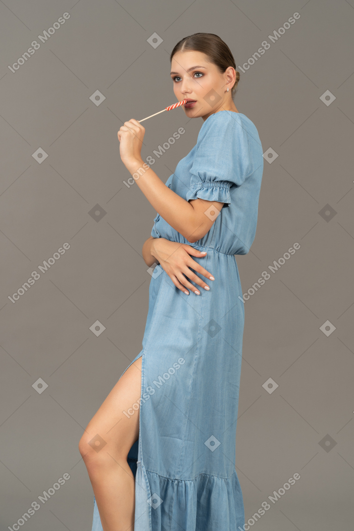 Vista de tres cuartos de una mujer joven en vestido azul sosteniendo una piruleta
