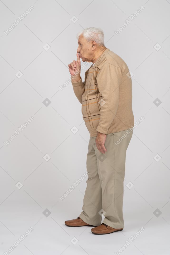Vue latérale d'un vieil homme en vêtements décontractés montrant le geste chut