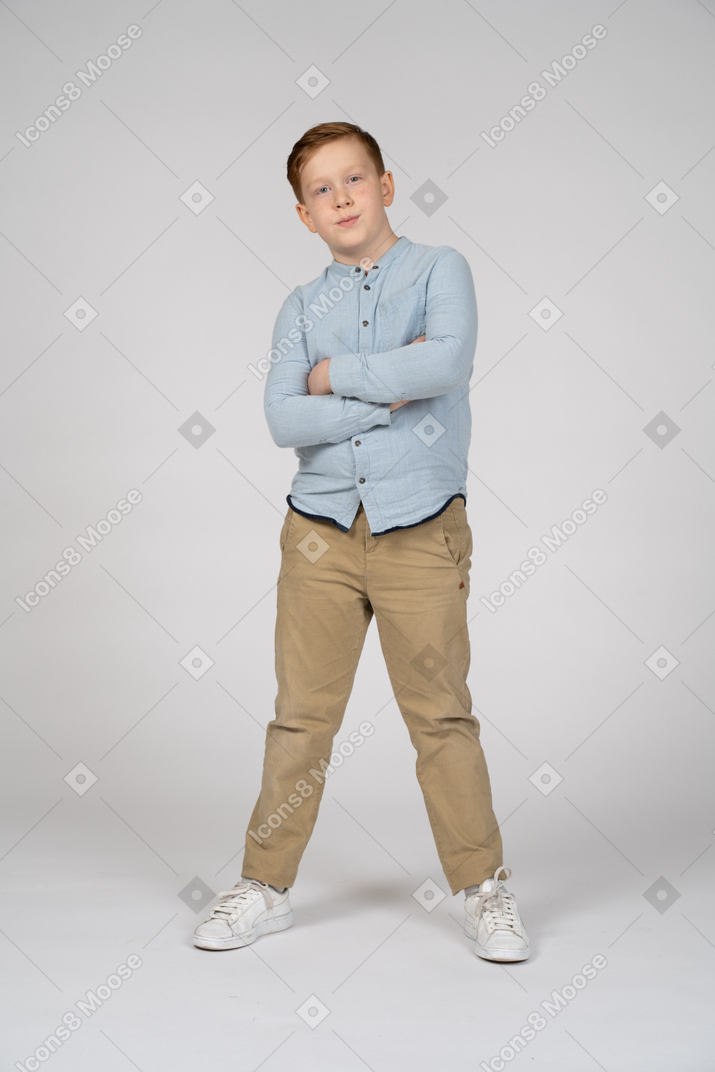 Vue de face d'un garçon mignon posant avec les bras croisés et regardant la caméra