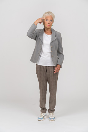 Front view of an old lady in suit touching forehead with finger