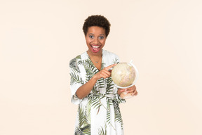 Black short-haired woman in a white and green dress, standing with a globe in her hand