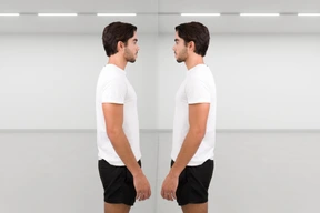 A pensive young man standing in front of his reflection