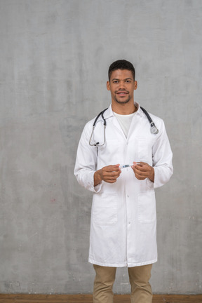 Médico varón sonriente sosteniendo un termómetro
