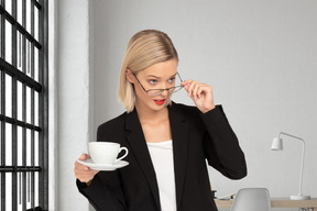 A woman holding a coffee cup and looking over glasses
