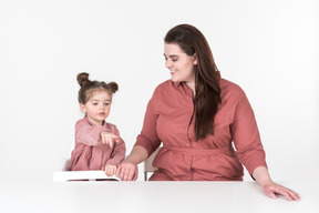 Mãe e sua filha, vestindo roupas vermelhas e rosa, sentado à mesa de jantar