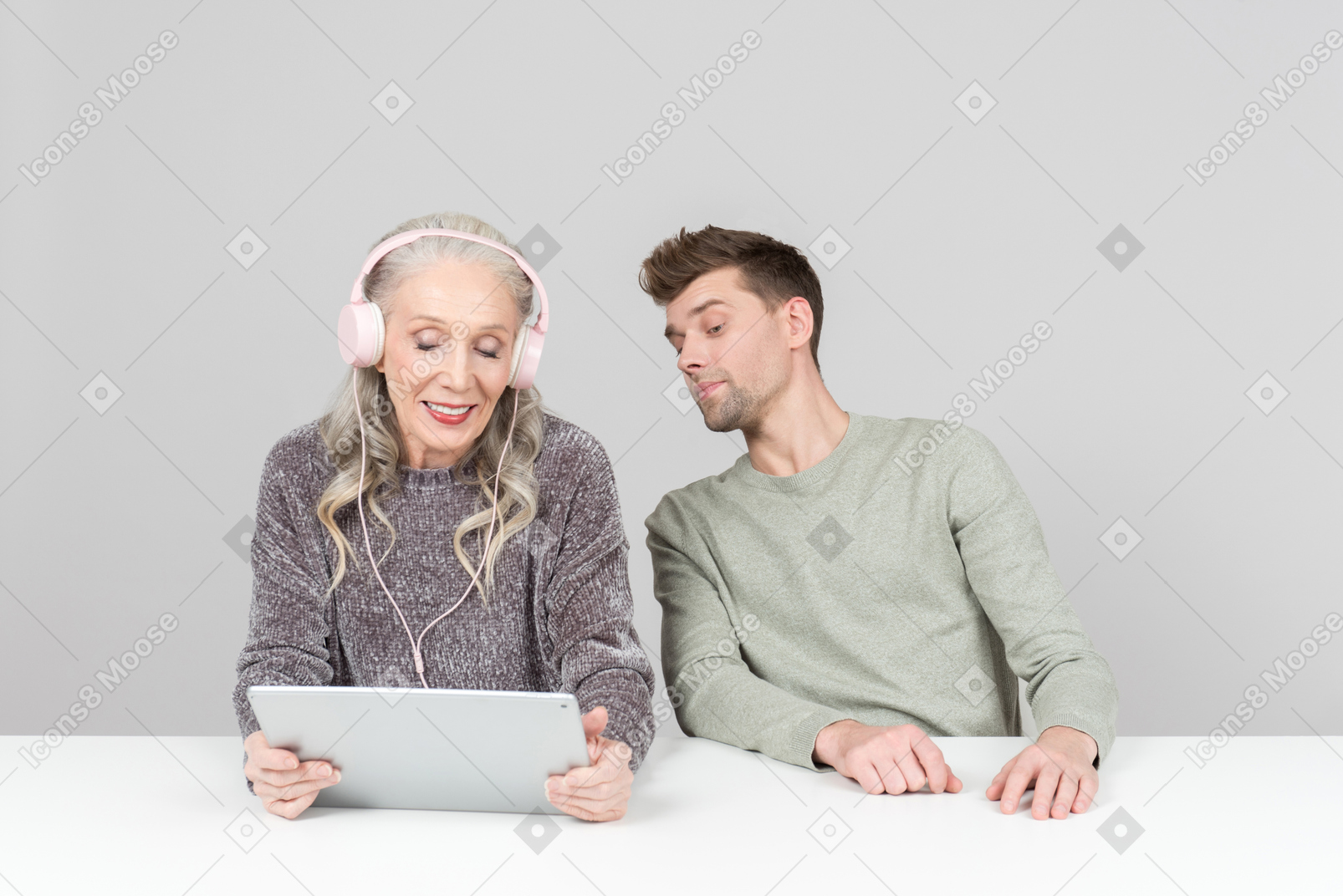 Old woman in headphones and young guy watching something on a digital tablet