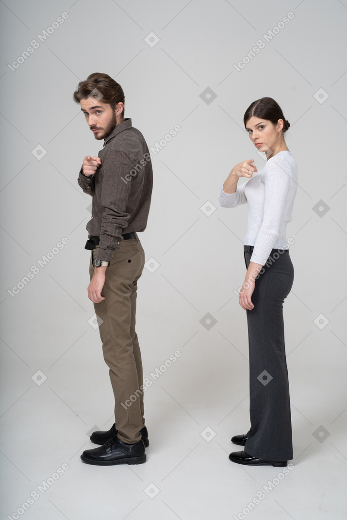 Side view of a young couple in office clothing pointing at camera
