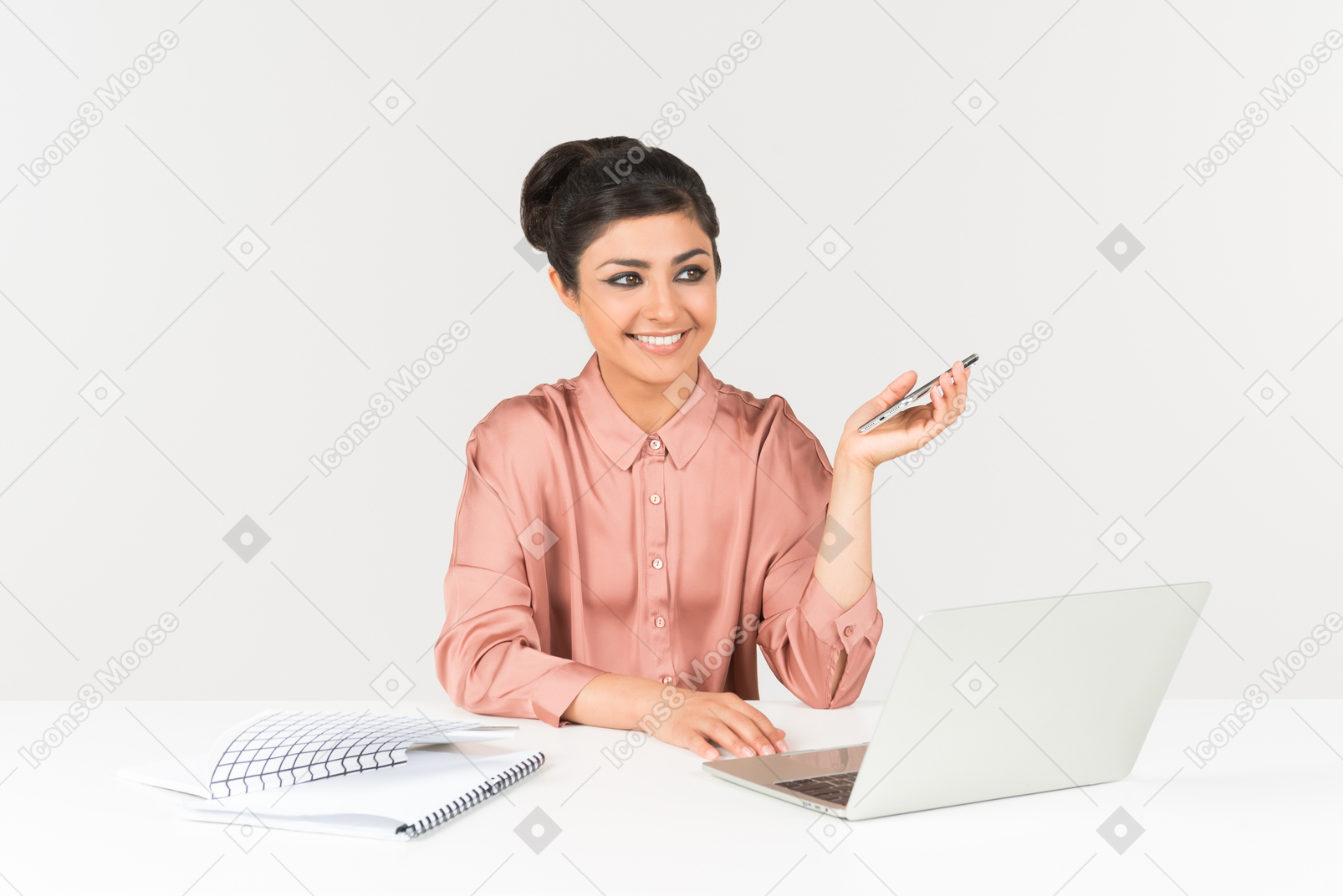 Smiling young indian woman holding phone and working on laptop
