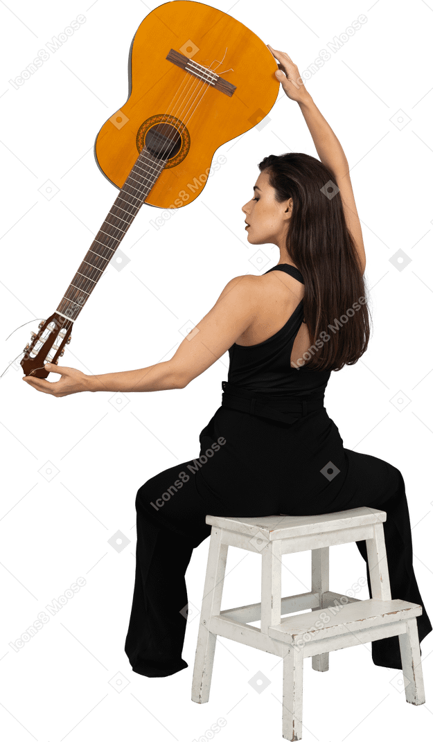 Vista traseira de uma jovem de terno preto segurando o violão de cabeça para baixo e sentada no banquinho