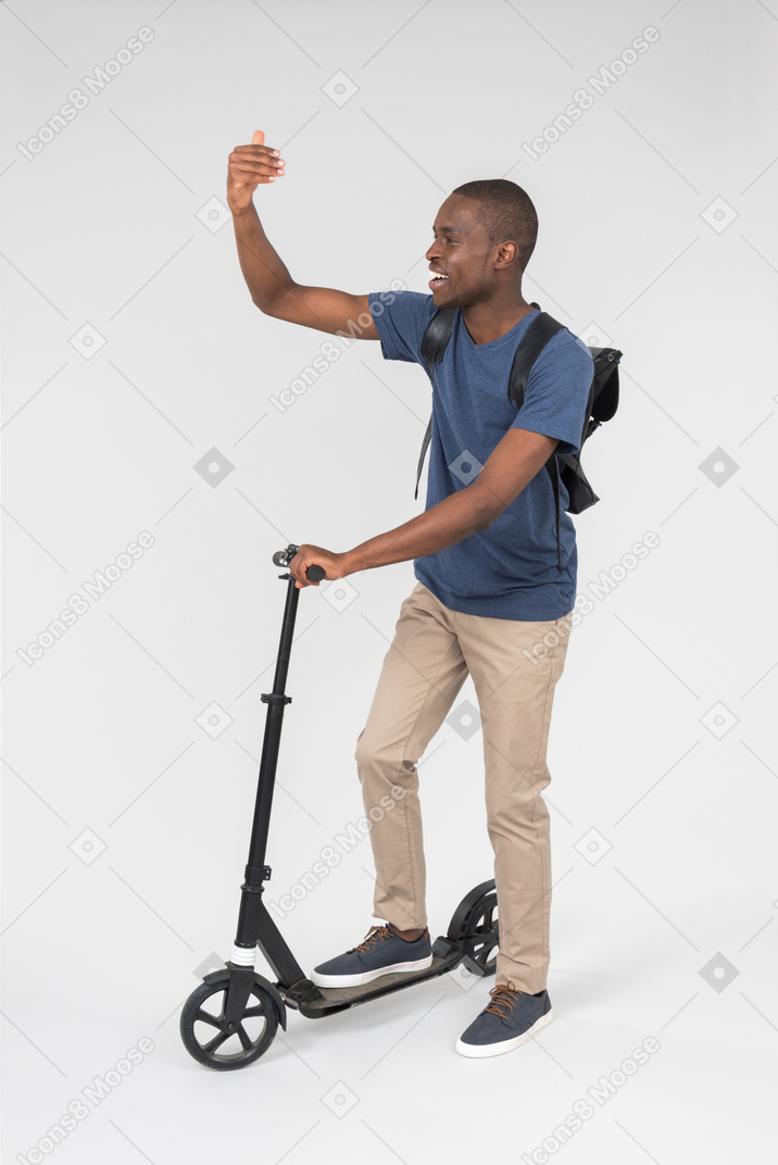 Black male city tourist using scooter and waving with a hand