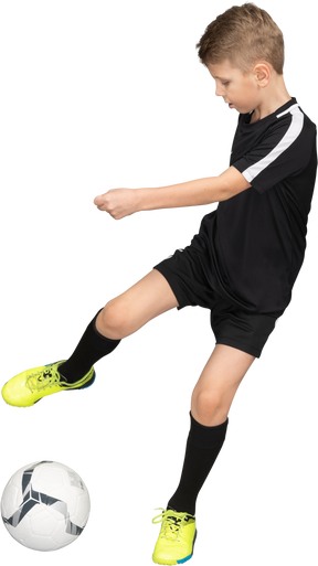 Vista frontale di un ragazzino in uniforme di calcio calciare una palla