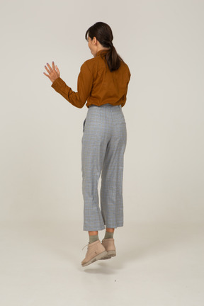Three-quarter back view of a jumping young asian female in breeches and blouse raising hands
