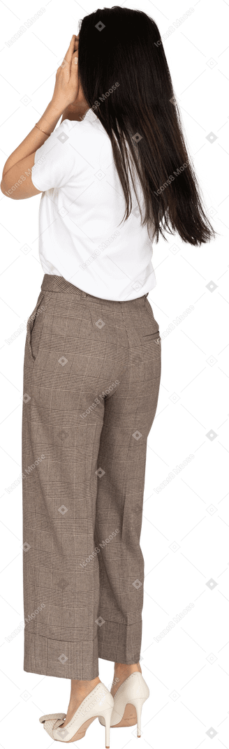 Vista posteriore di tre quarti di una giovane donna in calzoni e maglietta che nasconde il viso