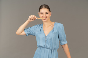 Front view of a young woman in blue dress brushing her teeth