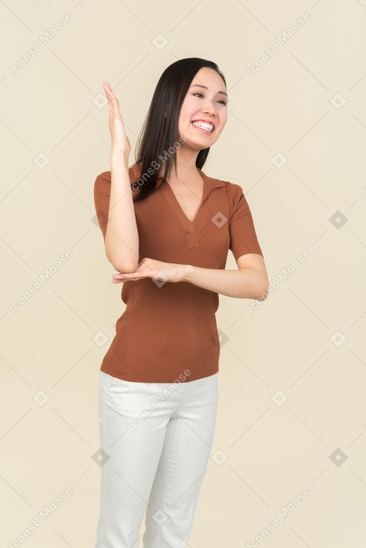 Smiling young asian woman holding one hand up