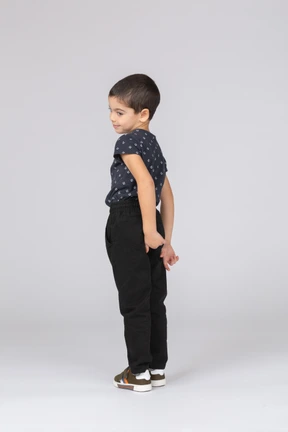 Side view of a shy boy in casual clothes standing with hands behind back and looking down