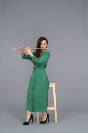 Comprimento total de uma jovem de vestido verde sentada em uma cadeira enquanto toca clarinete