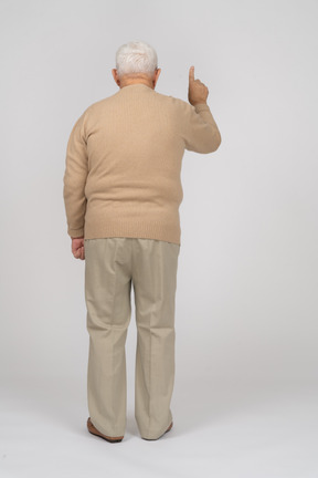 Vista trasera de un anciano con ropa informal apuntando hacia arriba con un dedo