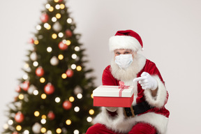 A man in face mask and a santa suit holding a box