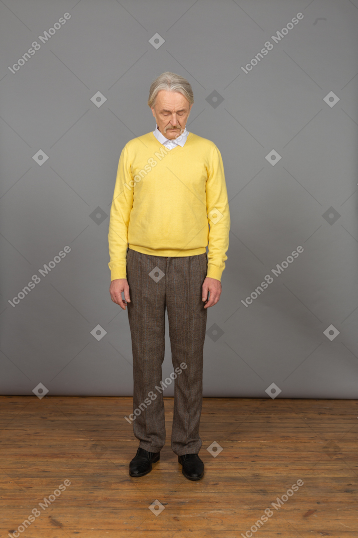 Front view of an old sad man in yellow pullover bending down with his eyes closed