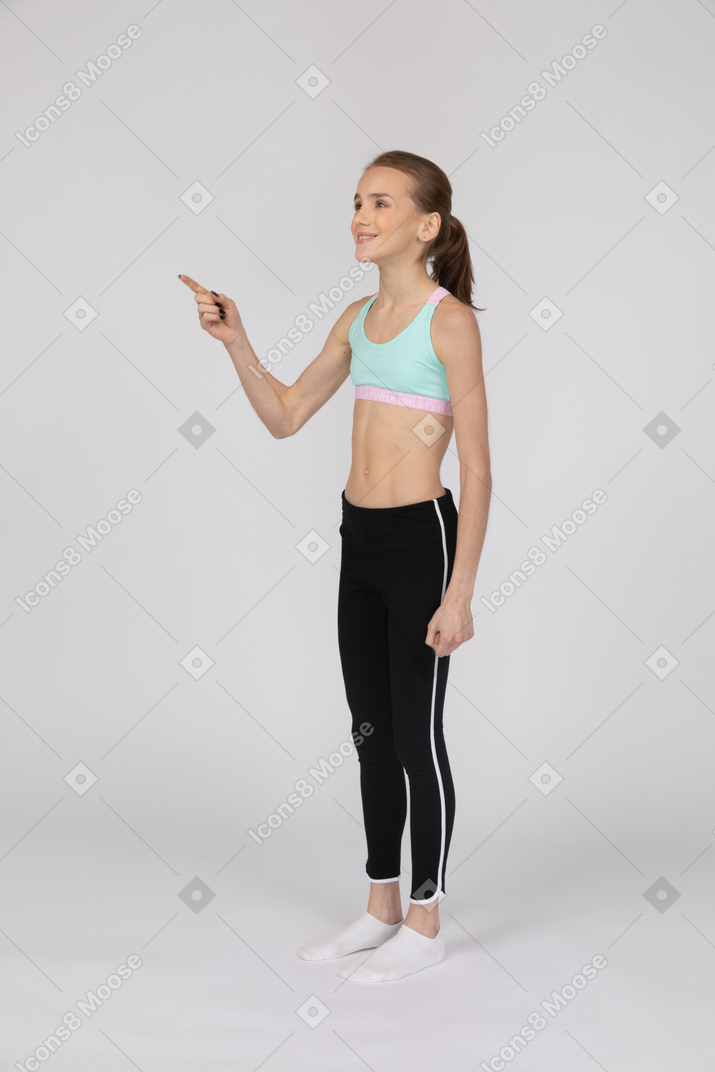 Three-quarter view of a teen girl in sportswear pointing finger and smiling