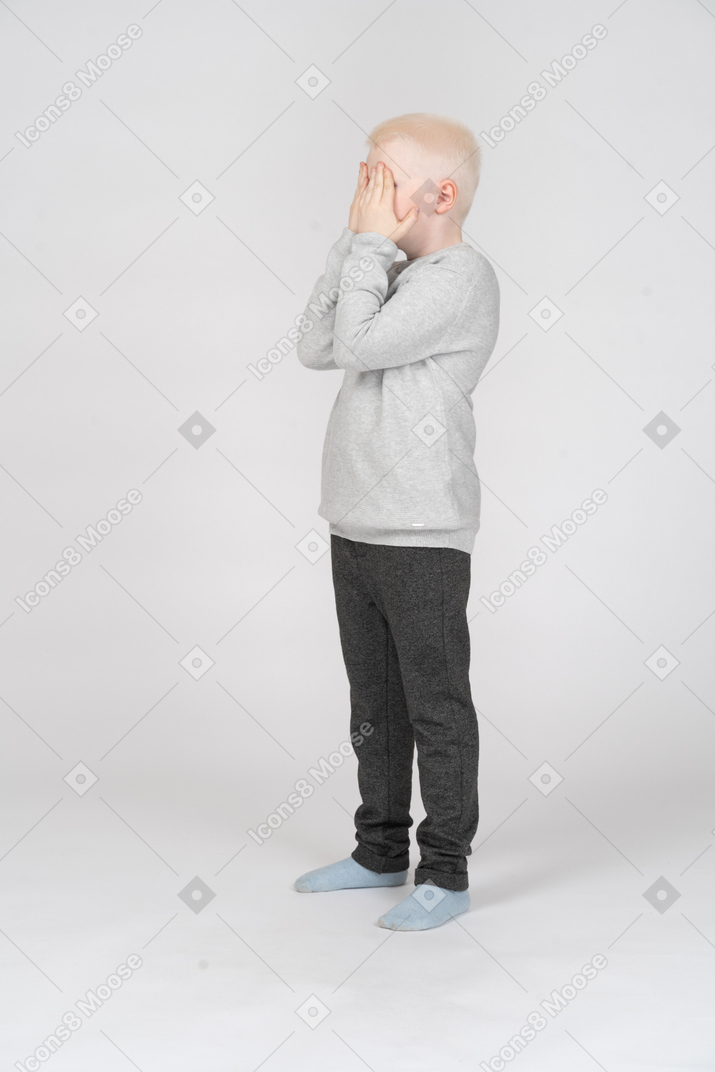 Side view of a little boy covering his face with hands