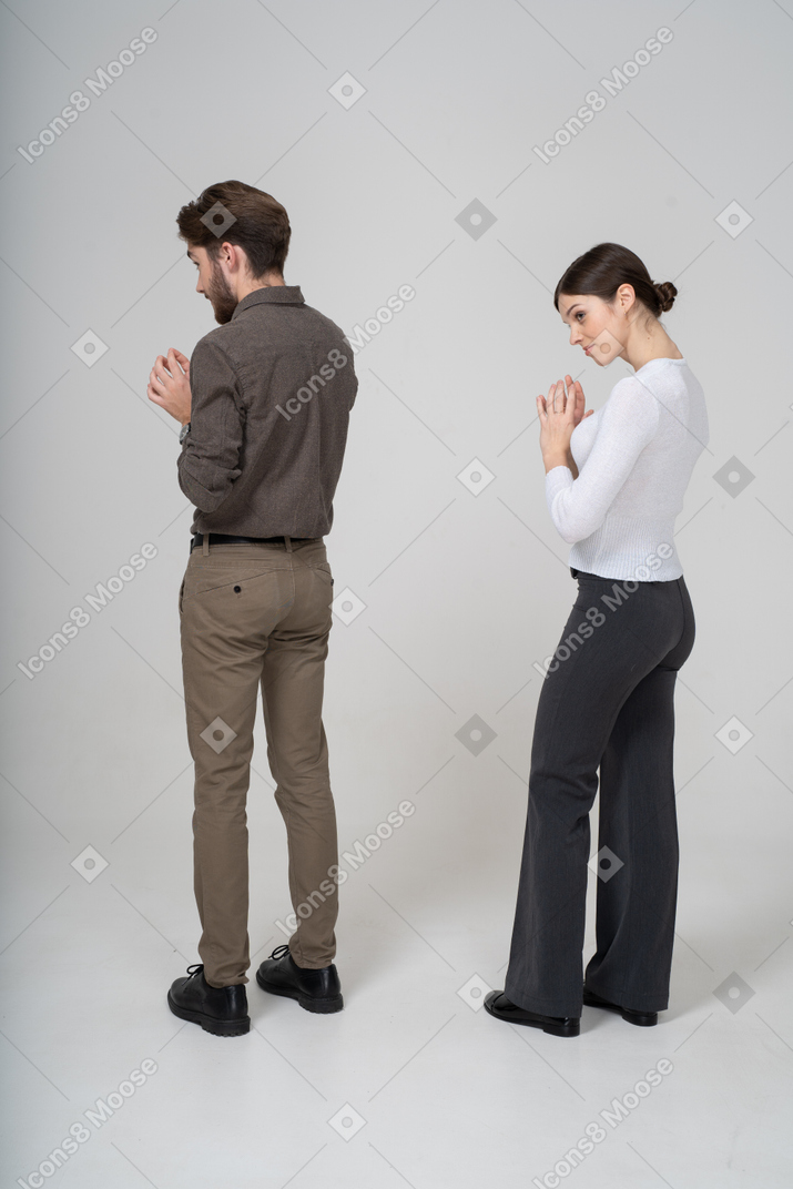 Вид сзади на три четверти хитрой молодой пары в офисной одежде, держащейся за руки