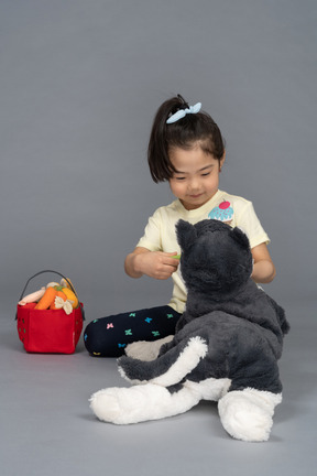 Retrato de una niña alimentando a un perro de peluche