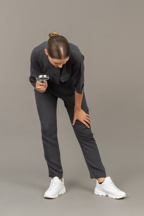 Front view of a young woman in a jumpsuit holding a magnifying glass