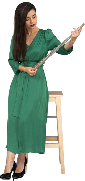 Front view of a young lady in green dress sitting on a chair and holding clarinet