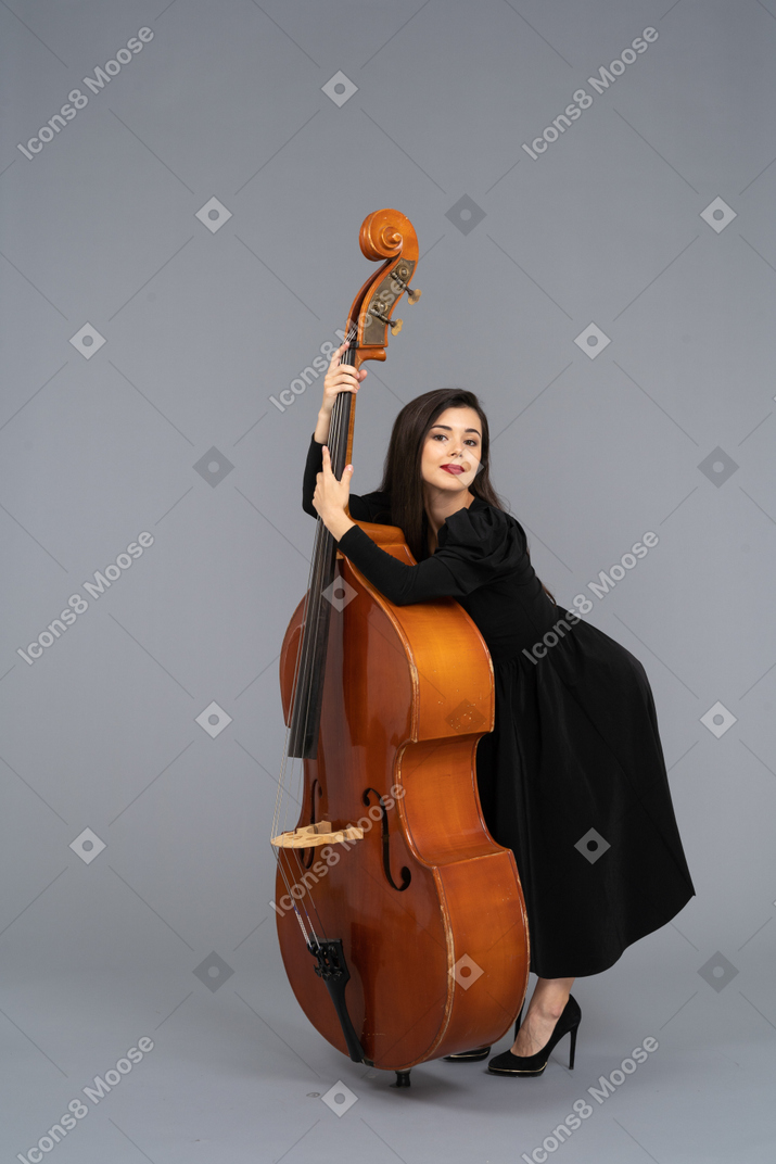 Three-quarter view of a young female musician in black dress holding her double-bass leaning forward