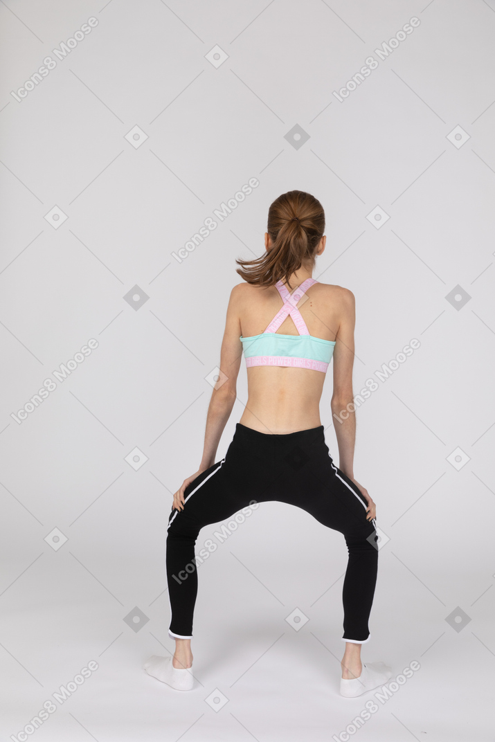Back view of a teen girl in sportswear squatting while putting hands on legs