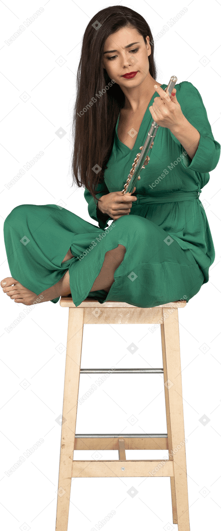 Toute la longueur d'une jeune femme tenant la clarinette assise, les jambes croisées sur une chaise en bois