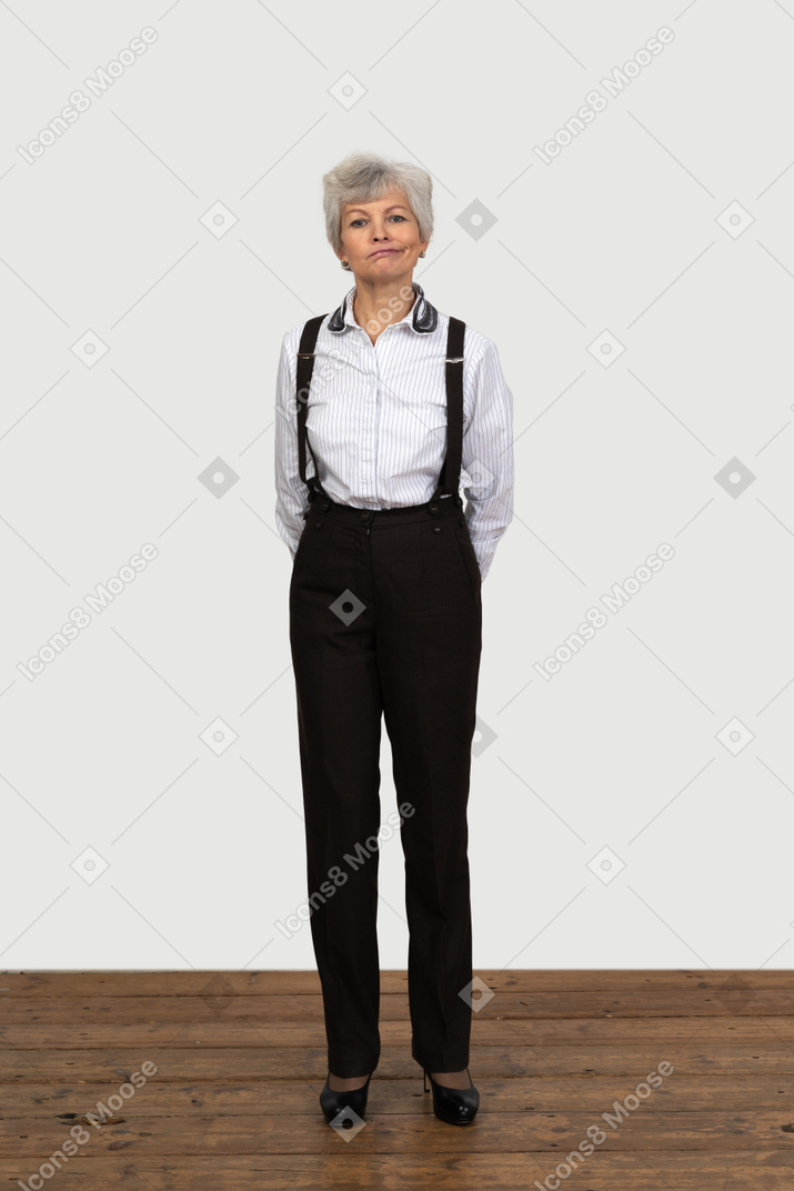 Vista frontale di una vecchia donna divertente in abiti da ufficio che fa smorfie con le mani dietro la schiena