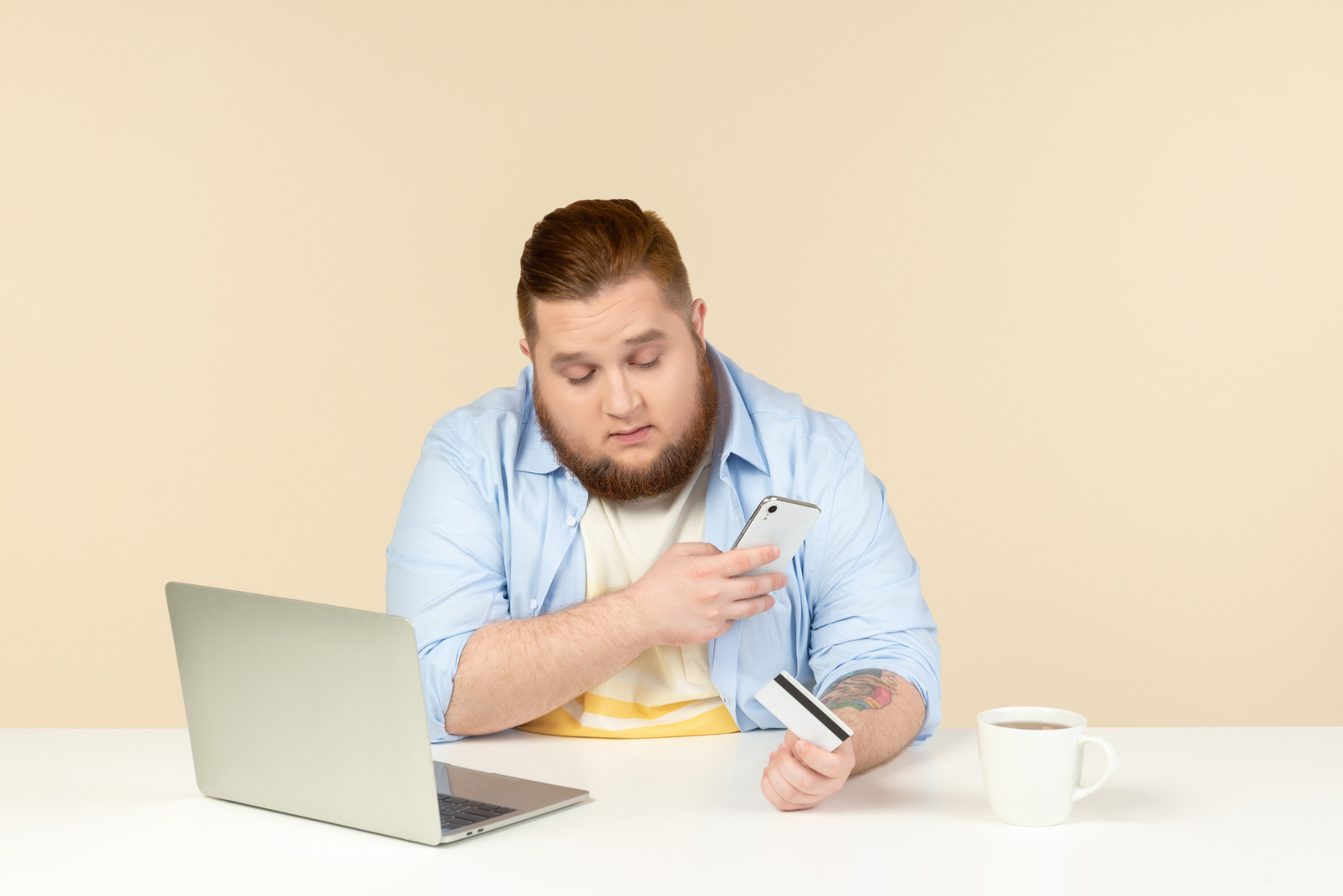 Young overweight man sitting at the table, using phone and doing online shopping