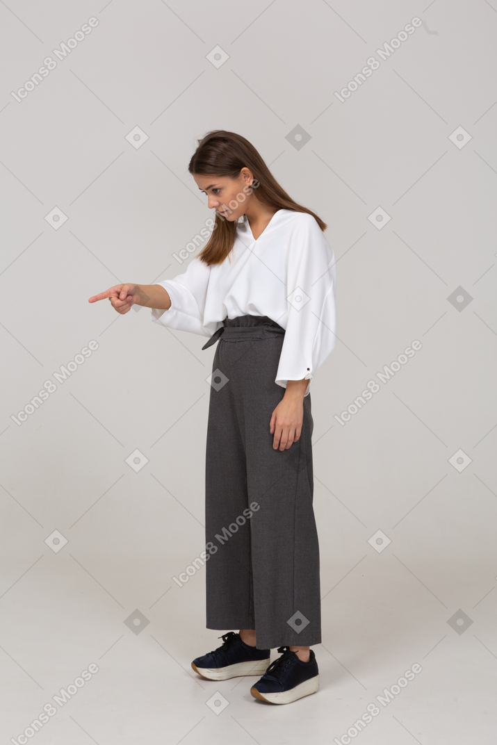 Трехчетвертный вид молодой леди в офисной одежде, указывающей пальцем