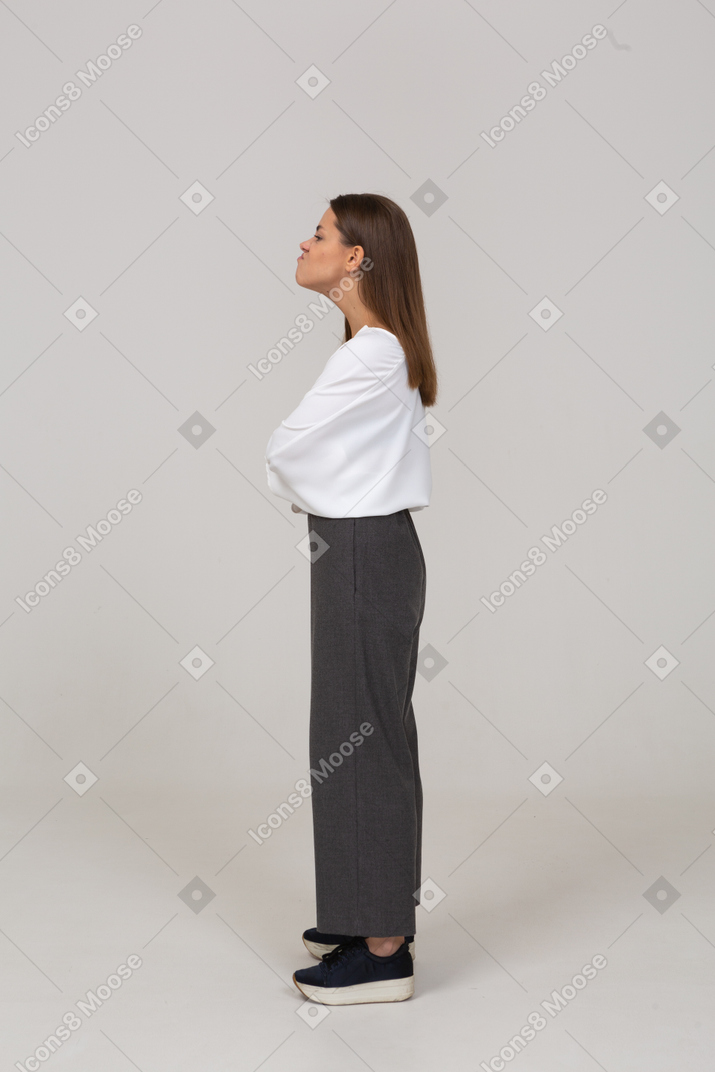Vista laterale di una giovane donna che fa smorfie in abiti da ufficio che incrociano le braccia