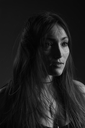 Noir three-quarter portrait of a young female with ethnic facial art and messy hair