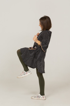 Side view of a happy little girl in dress clenching fists and raising leg