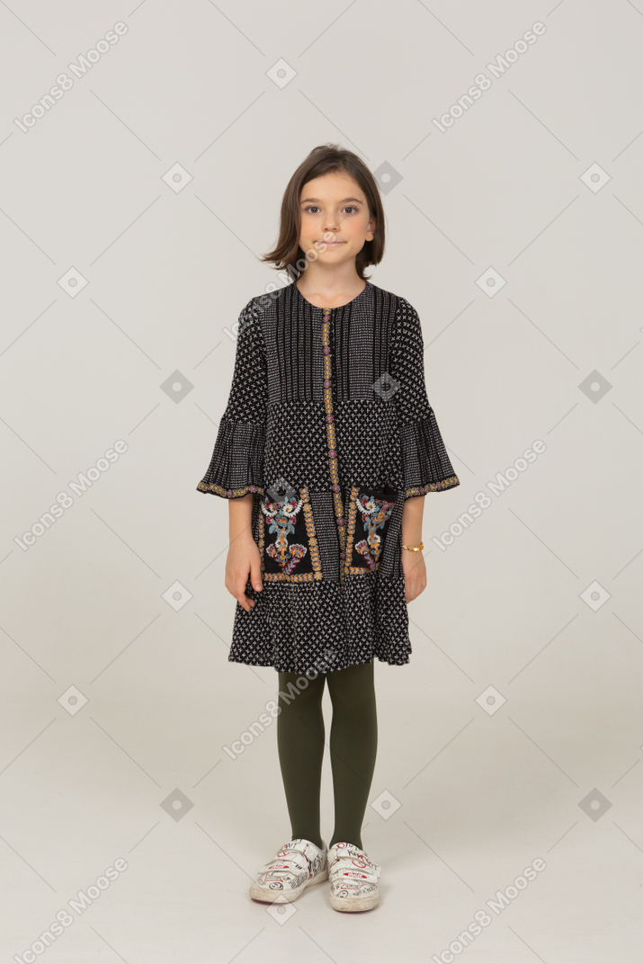 Vista frontal de una niña vestida de pie y mirando a la cámara