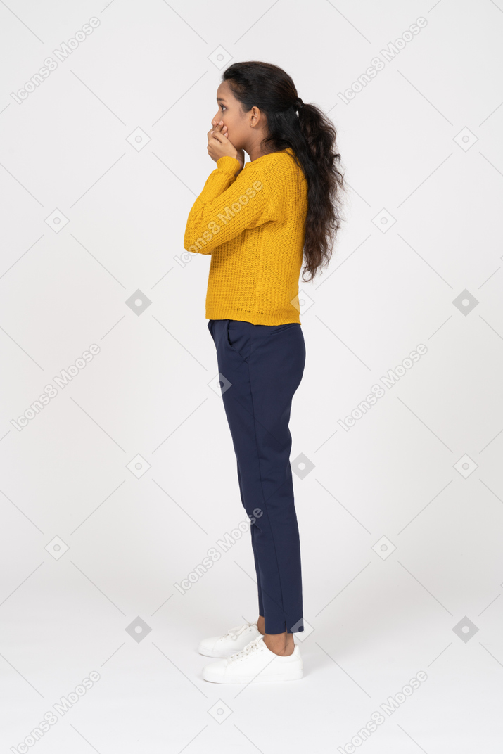 Vista lateral de una niña en ropa casual cubriendo la boca con las manos