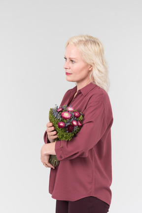 부르고뉴 셔츠를 입은 멋진 중년 금발 여성과 그녀의 손에 간단한 꽃 꽃다발