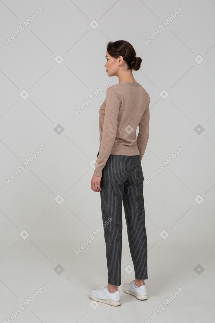 Three-quarter back view of a young lady standing still in pullover and pants