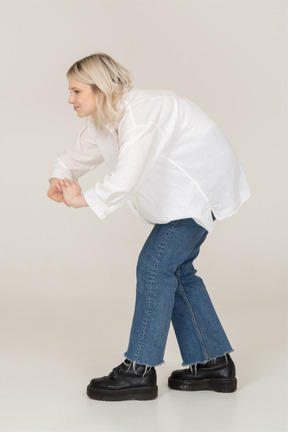 Vista lateral de uma mulher loira em roupas casuais, mostrando um gesto de coração ao se dobrar