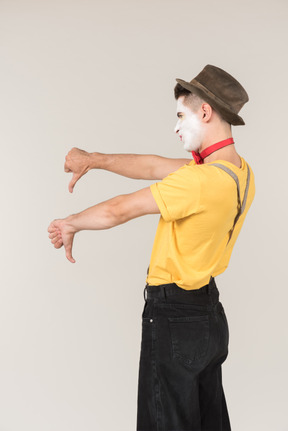 Sad looking male clown standing half sideways and showing thumbs down with both hands