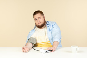 Preocupado buscando joven con sobrepeso sentado a la mesa y la presión sanguínea