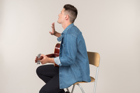 Young guy sitting on the table in profile and playing on guitar