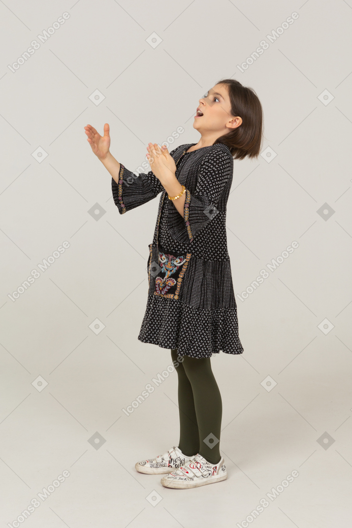 Vista lateral de una niña sorprendida en vestido extendiendo los brazos