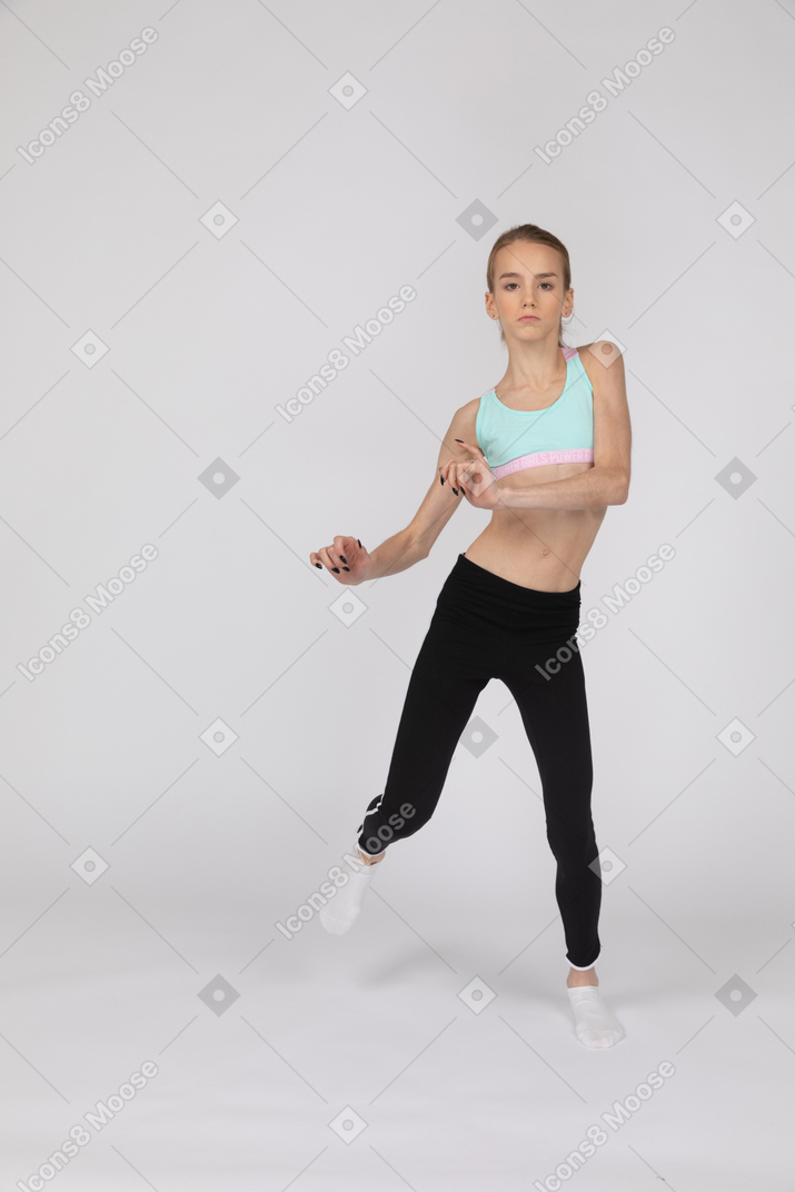 Vue de face d'une adolescente en tenue de sport en levant les mains et sa jambe en dansant